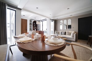 Un salon moderne avec une table à manger ronde dressée pour le repas, un canapé et une grande fenêtre avec des rideaux.