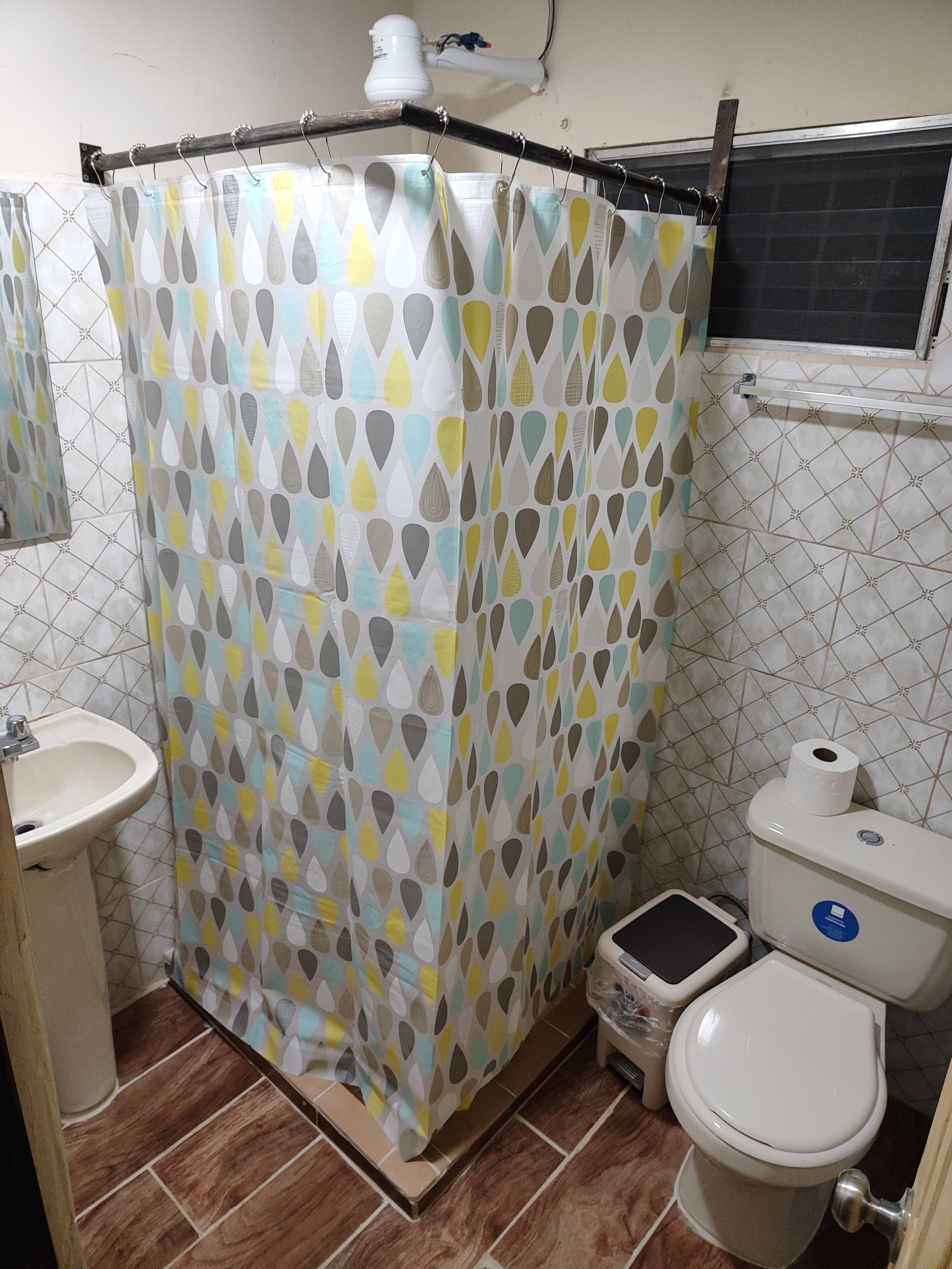A bathroom with a shower curtain featuring a geometric pattern, a sink, a toilet, and a small trash bin.