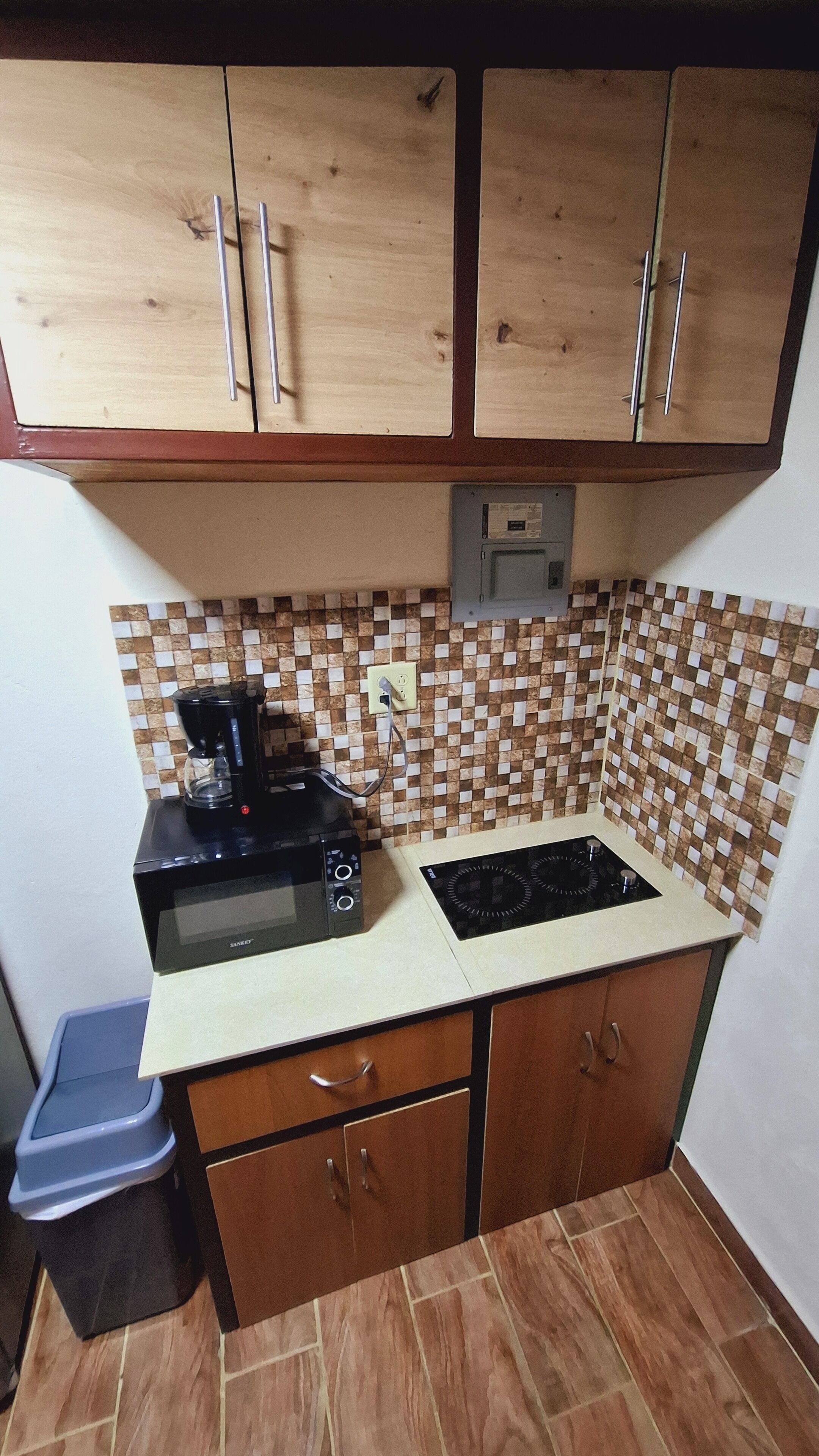 A compact kitchen with wooden cabinets, a microwave, a stove, and a coffee maker.