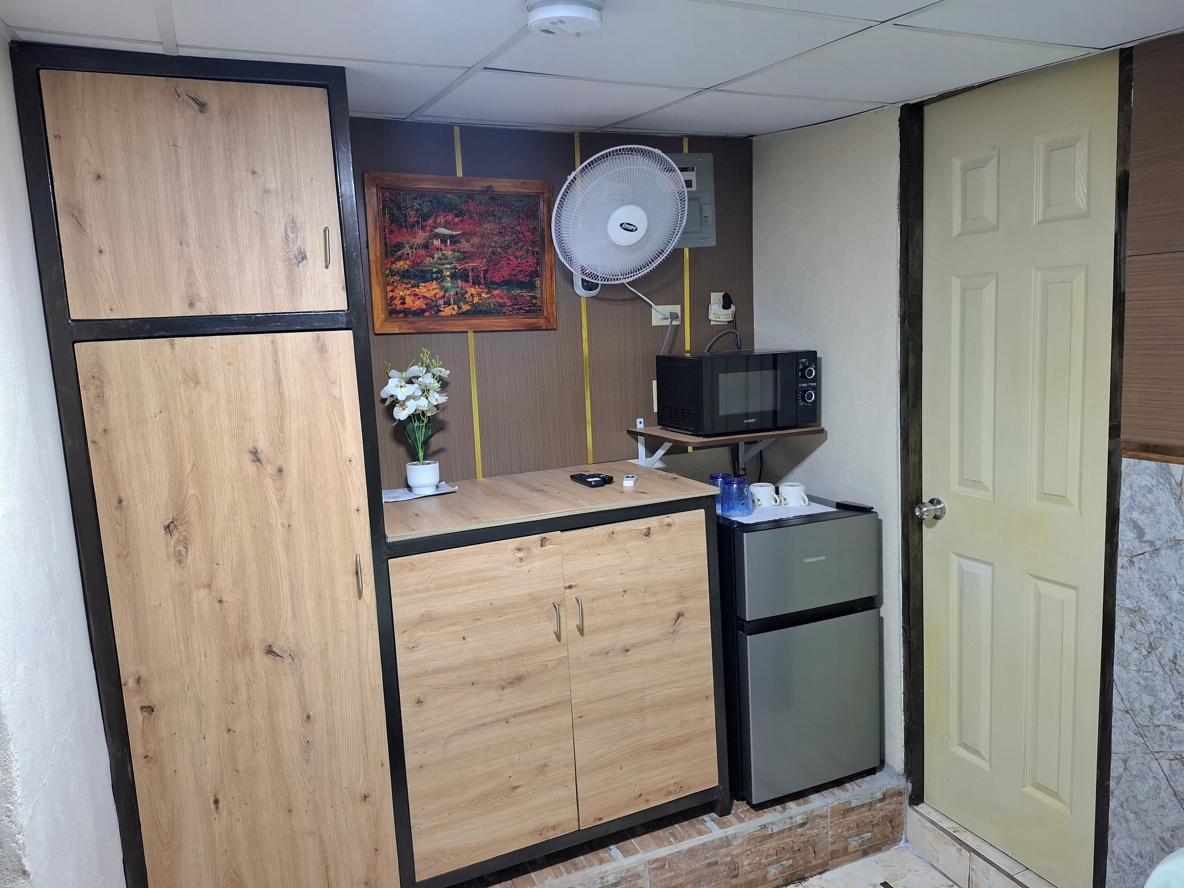 Una kitchenette compacta con microondas, un refrigerador pequeño y un mueble de madera.