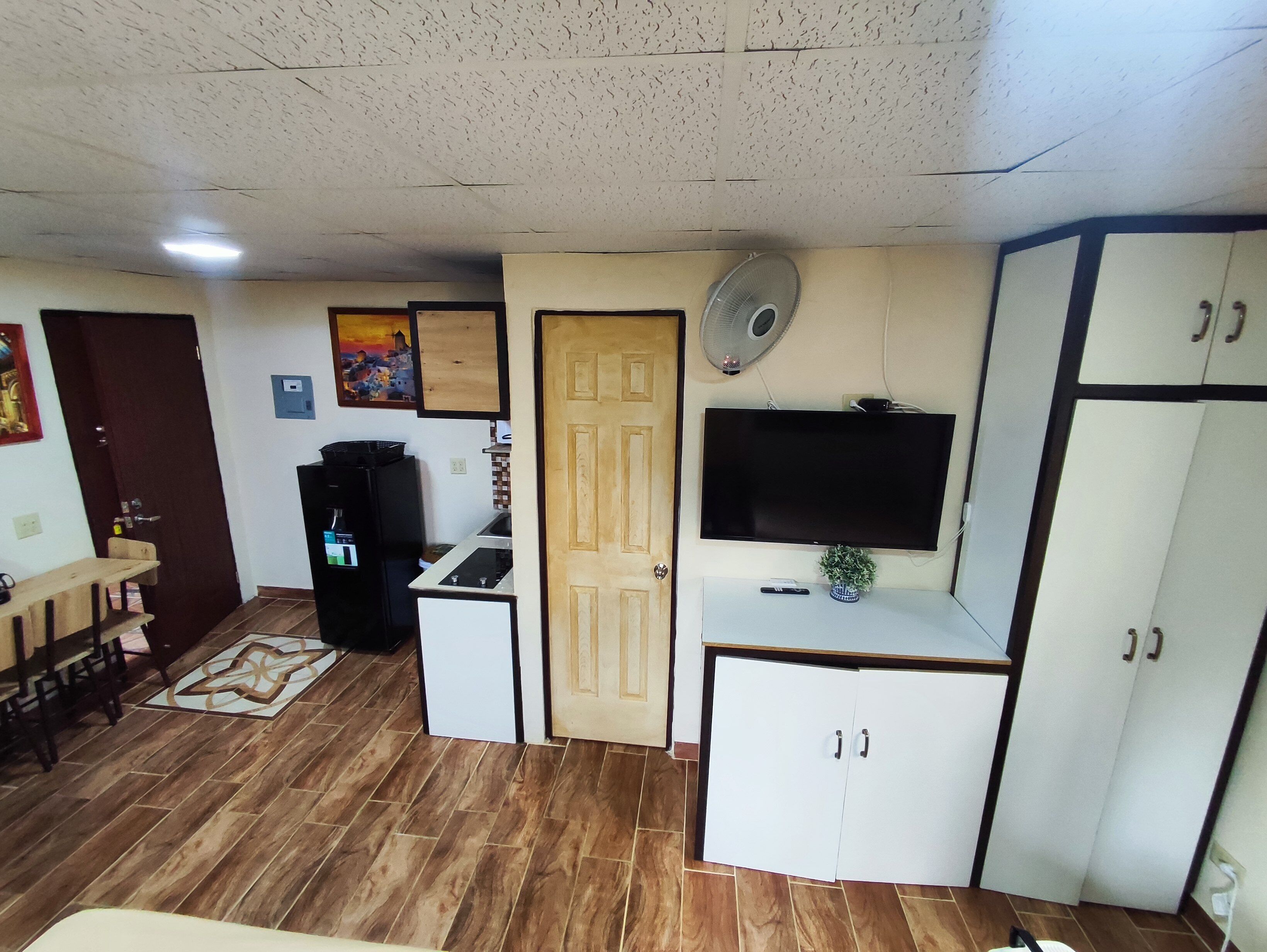 Un espacio habitable compacto con kitchenette, un televisor montado en la pared y un pequeño comedor.