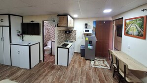A compact kitchen with a microwave, sink, and a refrigerator. There is a small dining area with a table and benches. The room has a tiled floor and a ceiling fan. - Aires frescos de Boquete (Alto Boquete)