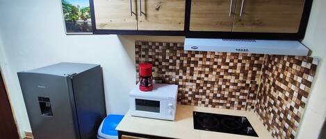 A compact kitchen with wooden cabinets, a microwave, a coffee maker, and a refrigerator.