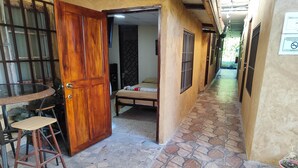 A corridor with a tiled floor, a wooden door, a bed, and a small table with a stool. - Aires frescos de Boquete (Alto Boquete)