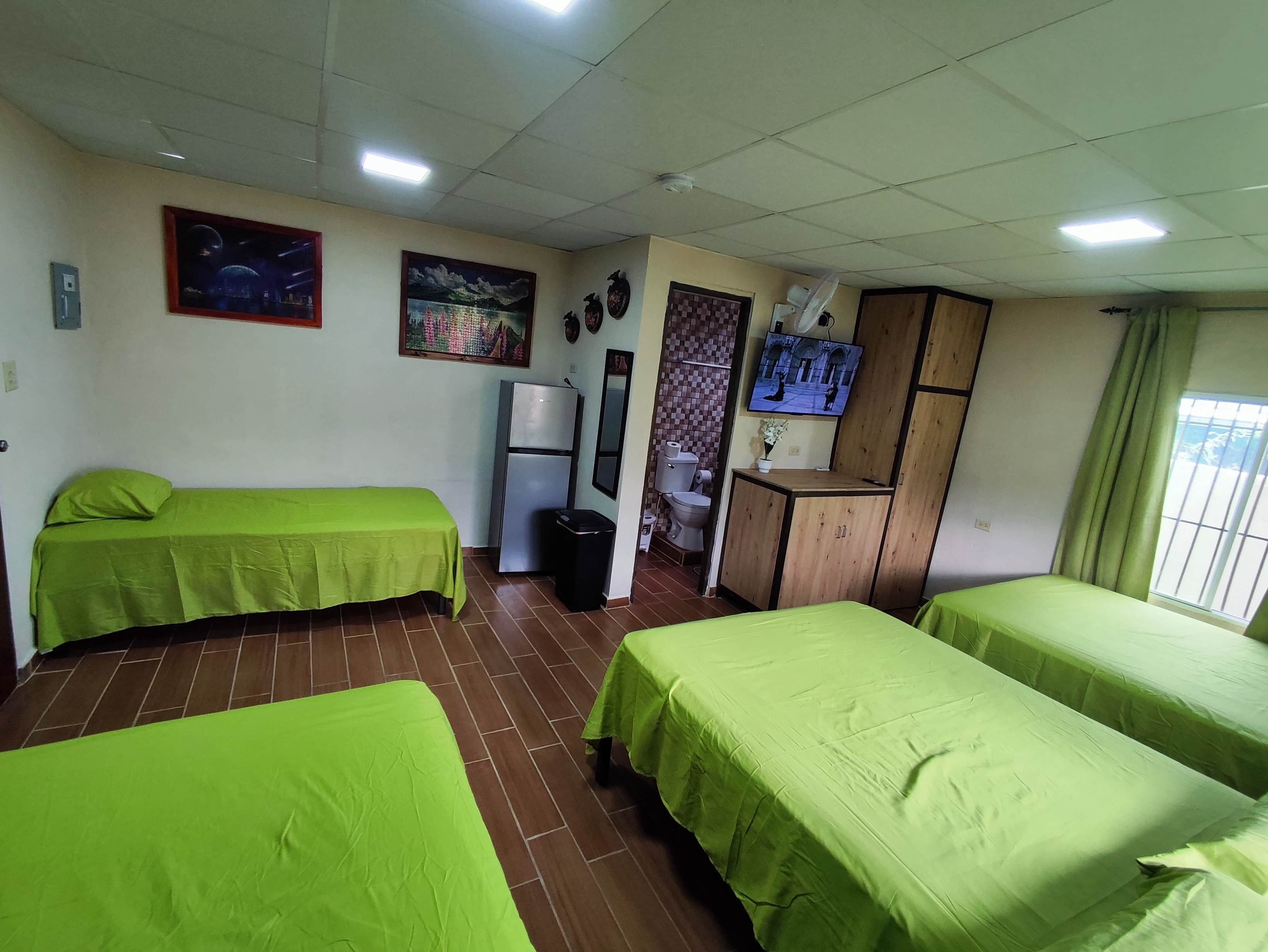 A room with two beds, a refrigerator, a television, and a window with curtains.