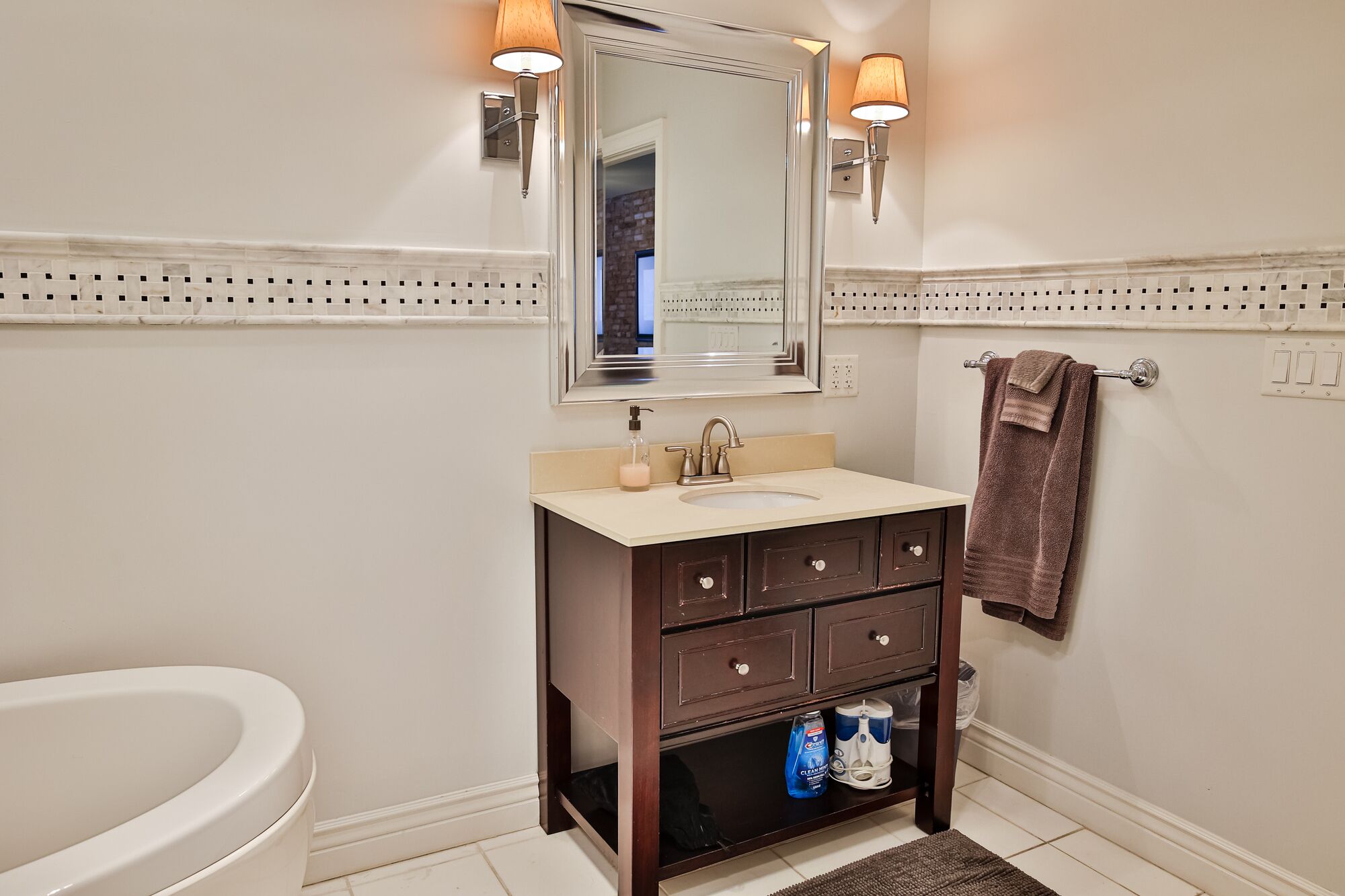 A bathroom with a white sink, dark wooden vanity, two wall-mounted lights, a mirror, and a towel rack.