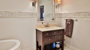 A bathroom with a white sink, dark wooden vanity, two wall-mounted lights, a mirror, and a towel rack.