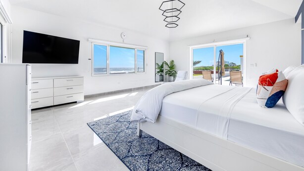 A modern bedroom with a large bed, a flat-screen TV, and a view of the outdoors. - Villa Farina in the Farrington (The Quarter)
