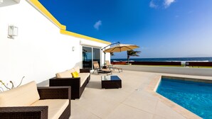 A poolside area with wicker furniture, a glass-enclosed patio, and a view of the ocean. - Villa Farina in the Farrington (The Quarter)