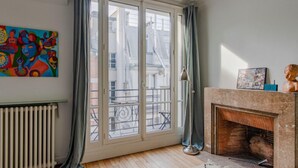 A room with a large window, a radiator, a fireplace, and a colorful abstract painting on the wall. - Courcelles Design Duplex (Paris)