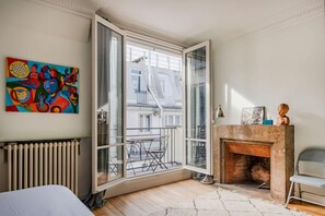 A room with a large window, a radiator, a fireplace, and a colorful abstract painting on the wall. - Courcelles Design Duplex (Paris)