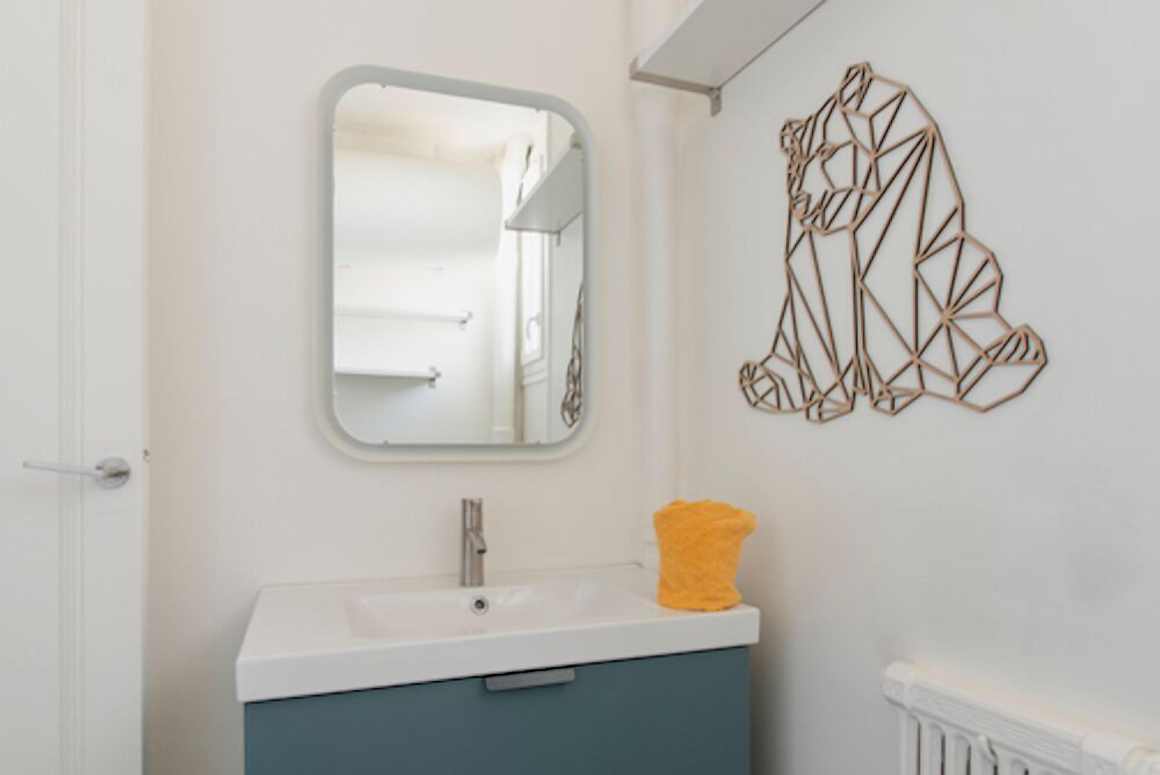 A bathroom with a white sink, a mirror, and a geometric wall decoration.