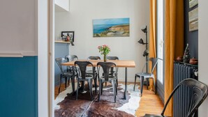 A dining area with a wooden table, six chairs, a cowhide rug, a painting of a coastal landscape, and a radiator. - Courcelles Design Duplex (Paris)