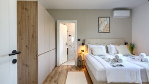 Une chambre à coucher comprenant un lit, des lampes de chevet, un climatiseur fixé au mur et une porte donnant sur une autre pièce.