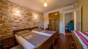 A bedroom with a stone wall, two beds, wooden wardrobe, and a small table with a vase.