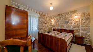 A bedroom with a stone wall, wooden bed, bedside table, and a small table with a vase. - Holiday Home Vintage by Villas Guide (Rab)