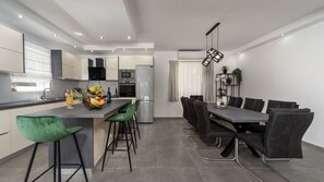 A modern kitchen with a central island, bar stools, a dining table with chairs, and a built-in oven. - Villa Danica by Villas Guide (Bibinje)