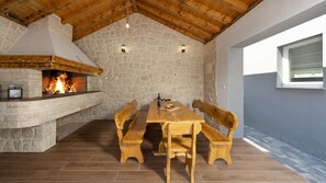 A stone fireplace with a fire, wooden benches, and a table with wine glasses and bottles. - Villa Danica by Villas Guide (Bibinje)