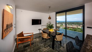 A modern room with a dining table, chairs, a TV, and a large window with a city view.