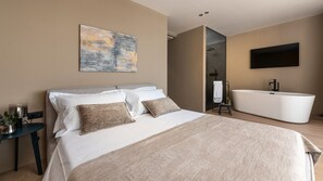 Una moderna camera d'hotel con un letto grande, una vasca da bagno, un televisore a schermo piatto e un quadro appeso al muro.