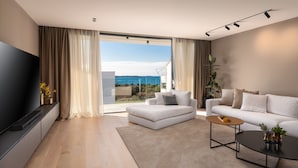 A modern living room with a large TV, a sofa, a coffee table, and a view of the sea. - Villa Aruna by Villas Guide (Pula)
