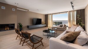 A modern living room with a sofa, coffee table, and TV. There is a fireplace, large windows, and a balcony. - Villa Aruna by Villas Guide (Pula)