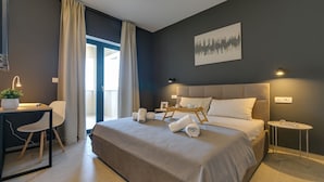 Ein modernes Hotelzimmer mit einem großen Bett, einem Schreibtisch, einem Sessel und einem Nachttisch, mit Blick ins Freie.