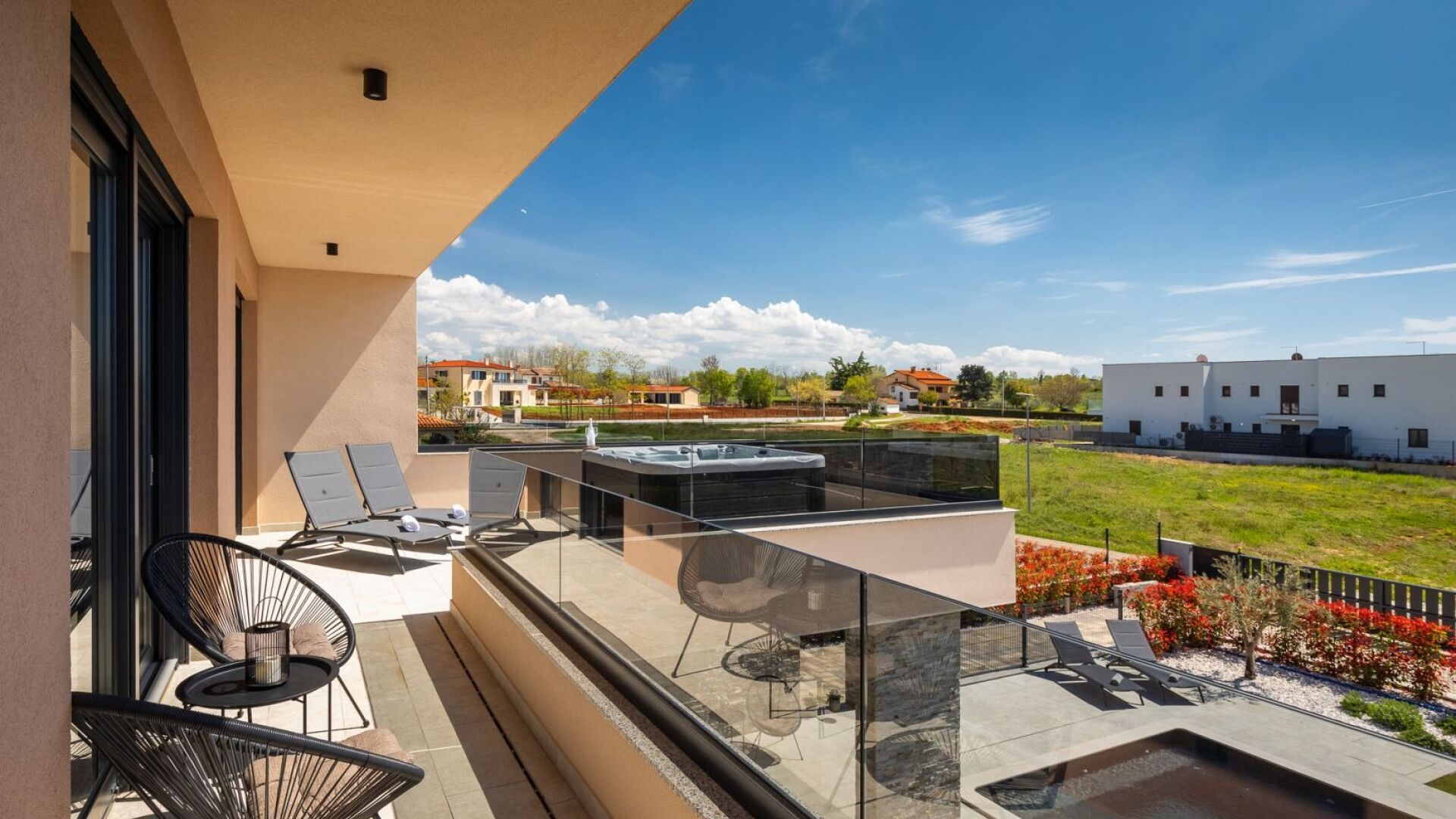 A balcony with a glass balustrade, outdoor seating, and a hot tub.