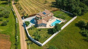 A large house with a swimming pool, surrounded by a well-maintained lawn and fields.