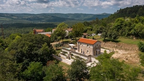 A rural house with a stone facade and red-tiled roof, surrounded by lush greenery and hills in the background. - Villa Casa Mavretici by Villas Guide (Livade)