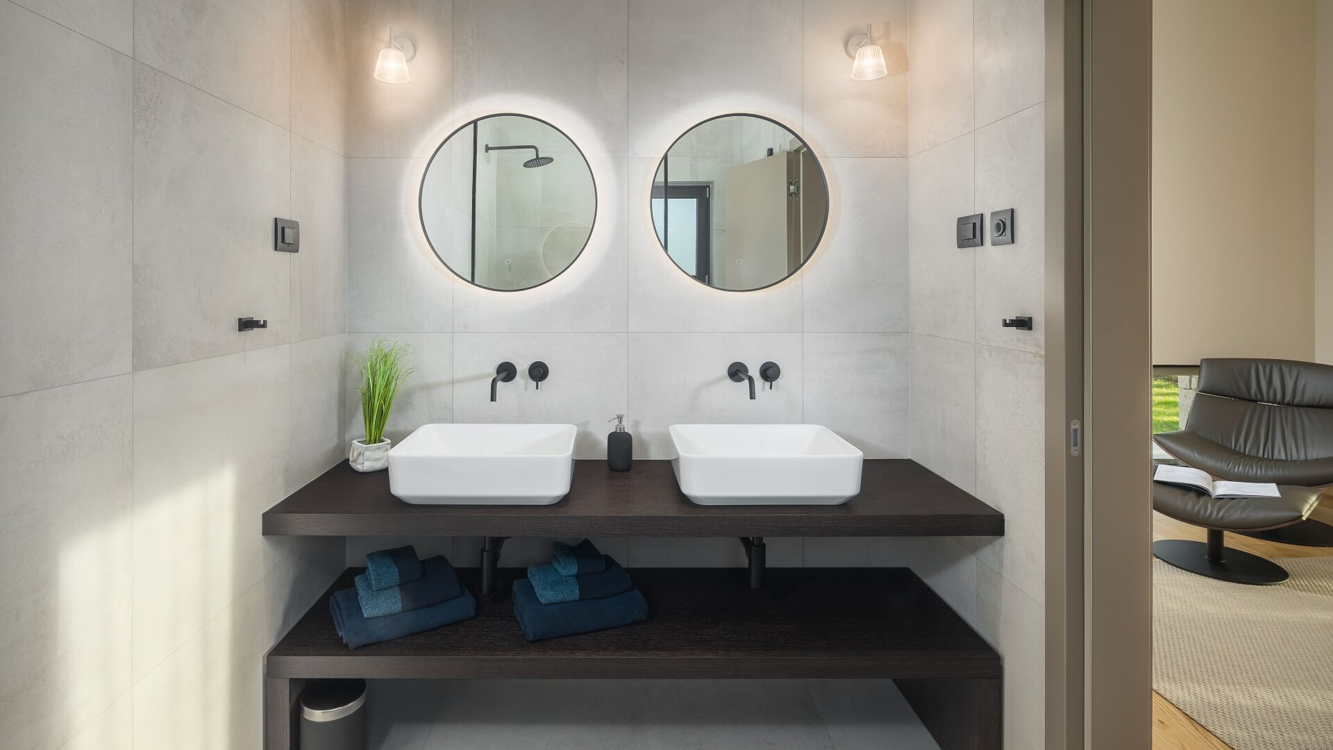 A modern bathroom with two sinks, a mirror, and a bench below.