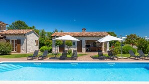 A poolside area with lounge chairs and umbrellas, a stone building with a tiled roof, and a clear blue sky. - Villa St. Martina by Villas Guide (Kringa)