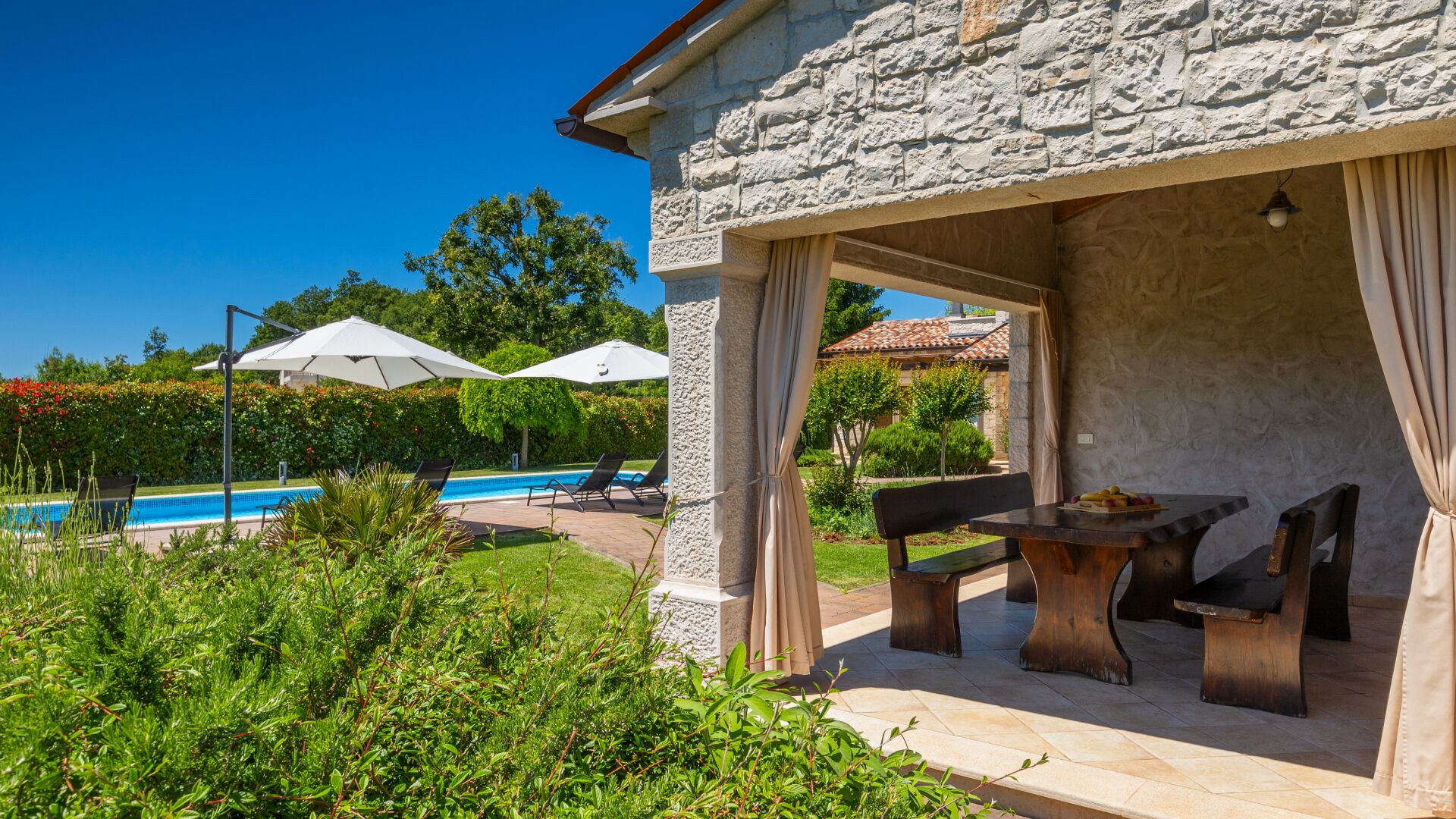 A stone building with a pool, outdoor seating, and umbrellas.