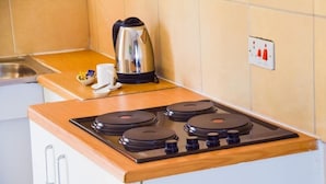 A compact kitchenette with a four-burner gas stove, a kettle, and a coffee maker on the countertop. - Tudu Guest House (Jwaneng)