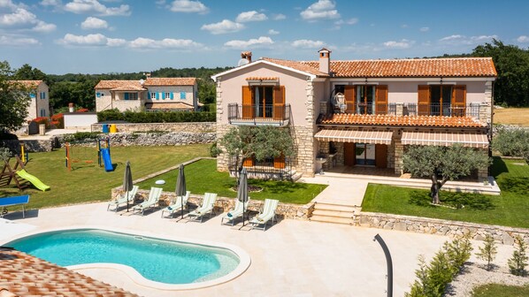 A villa with a swimming pool, outdoor seating, and a garden.