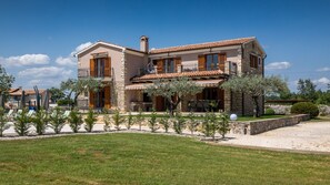 Una casa a due piani con facciata in pietra, diversi balconi e un prato curato.