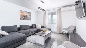 Een moderne woonkamer met een grijze modulaire bank, een witte salontafel, een grijze fauteuil en een aan de muur bevestigde televisie.