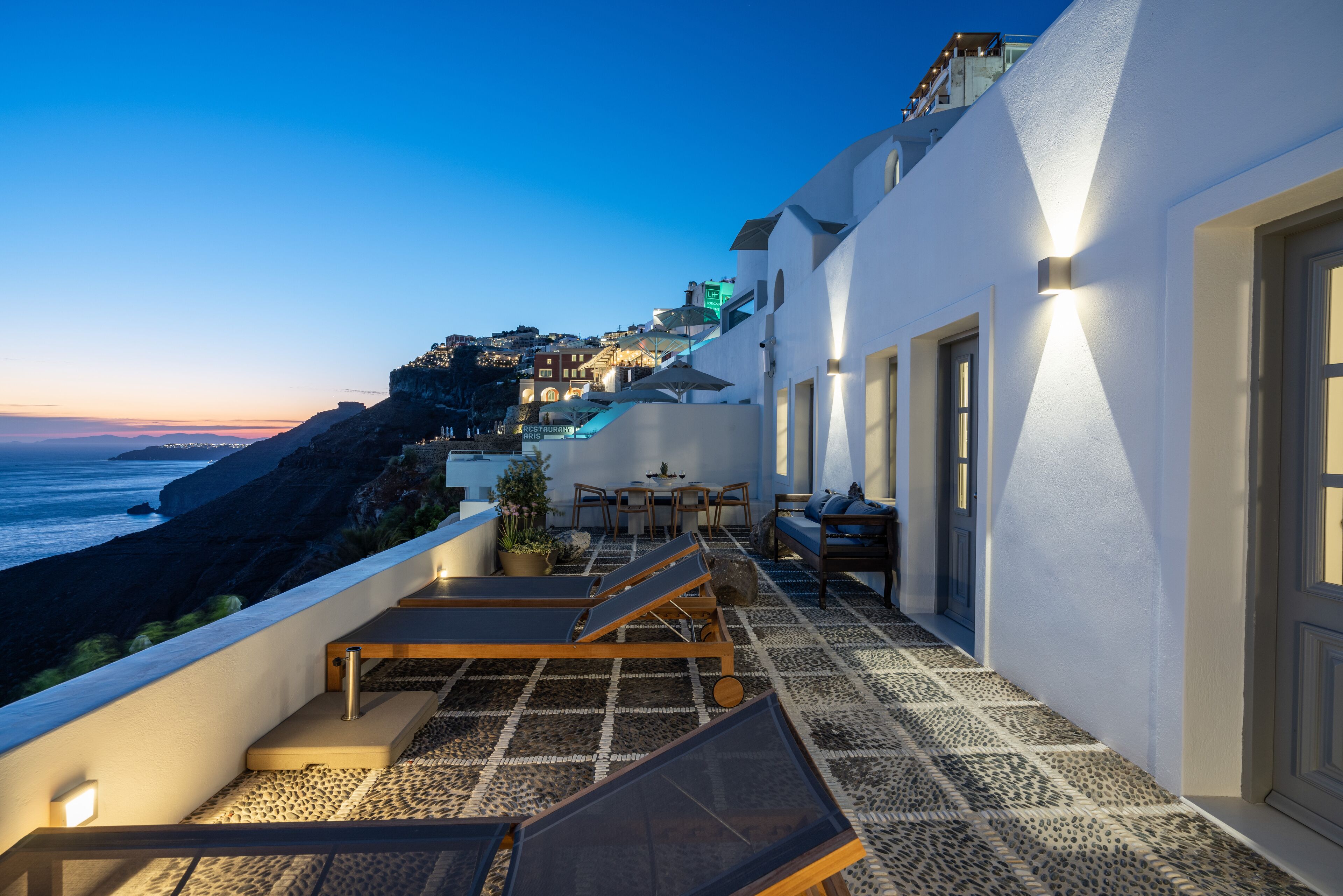 A rooftop terrace with sun loungers, a dining area, and a view of the ocean.