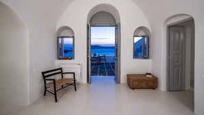 A hallway with white walls, an arched doorway leading to a balcony with a view of the sea.