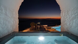 A hot tub with a sunset view, a small table with a glass of wine, and a bowl of grapes.