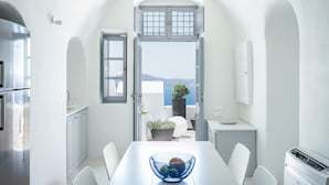 A modern kitchen with white cabinetry, a dining table with chairs, a blue bowl, and a view of the sea through an open door.