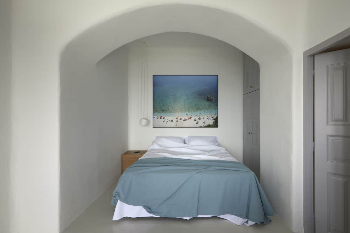 Un dormitorio con cama, mesita de noche, un cuadro de una playa y una puerta.
