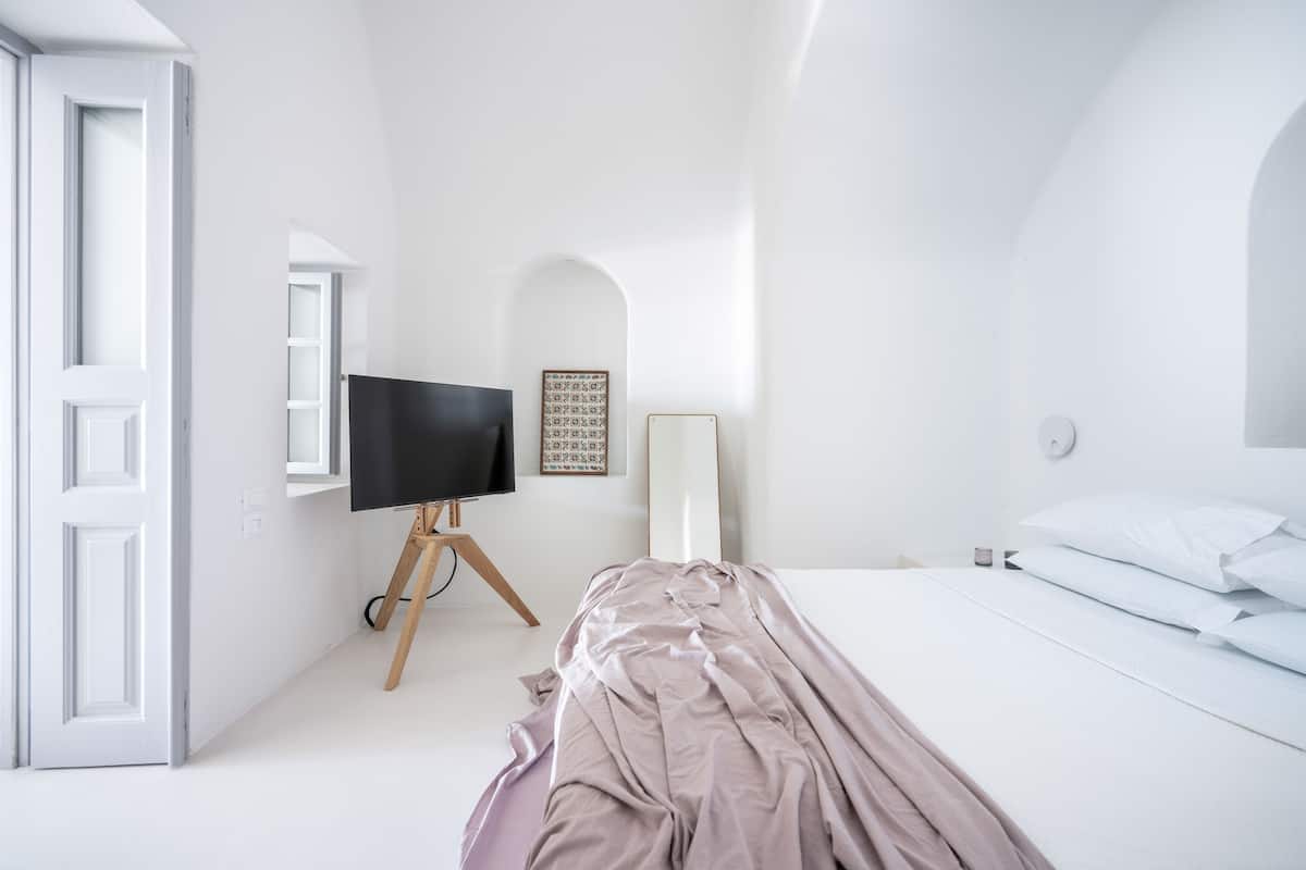 Un dormitorio minimalista con una cama, un televisor sobre un mueble bajo y un cuadro en la pared.