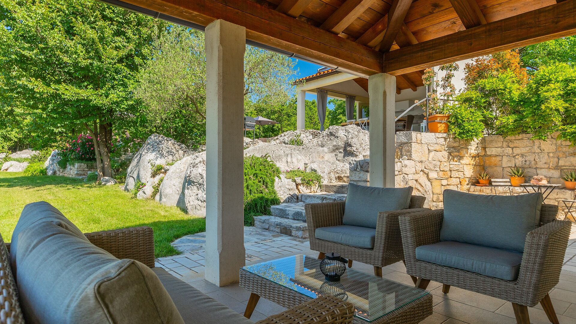 Un espace extérieur aménagé en terrasse, avec des meubles en osier, une table basse en verre et un mur en pierre en arrière-plan.
