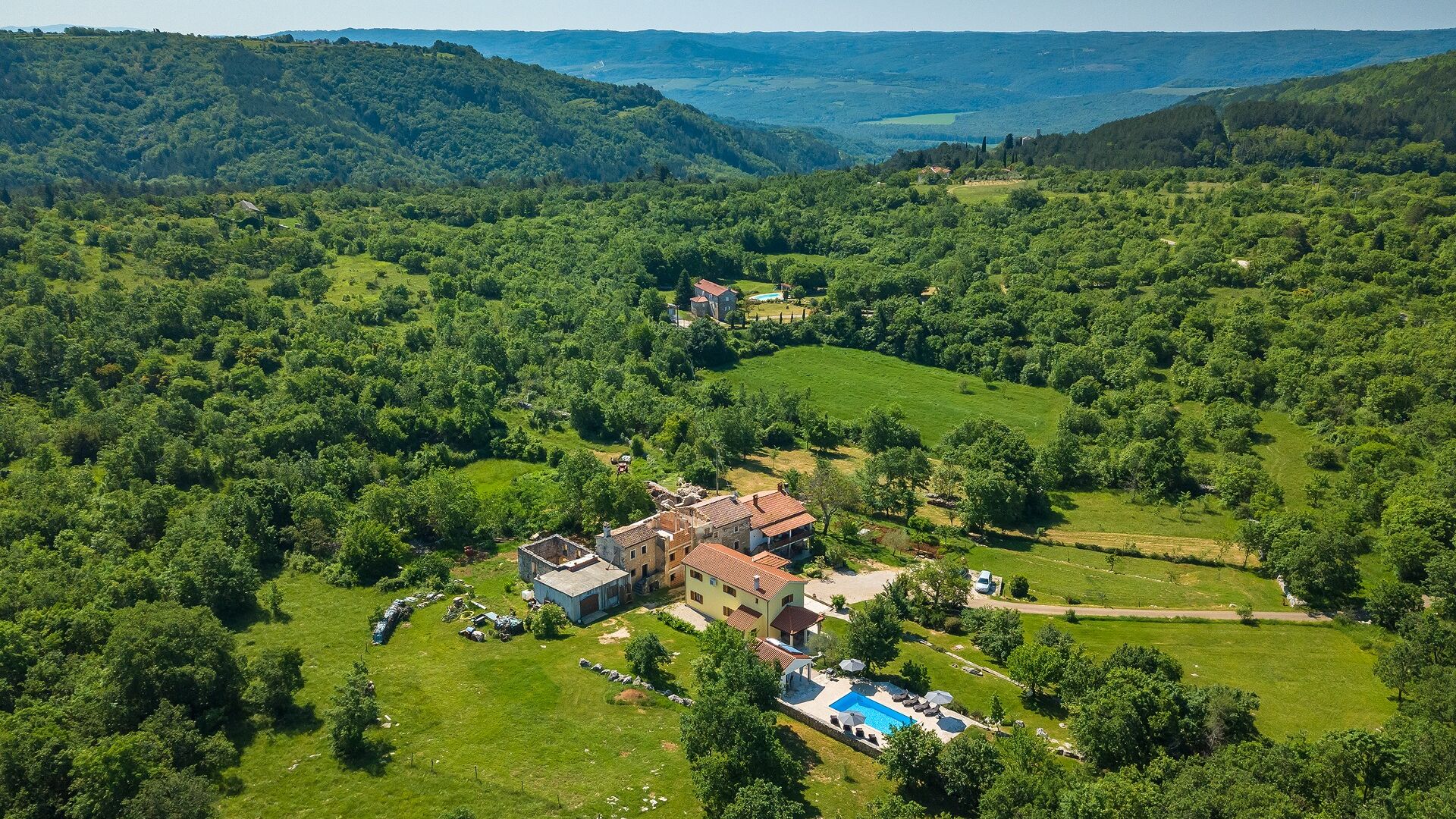 An aerial view of a rural property with multiple buildings, a swimming pool, and surrounding greenery.