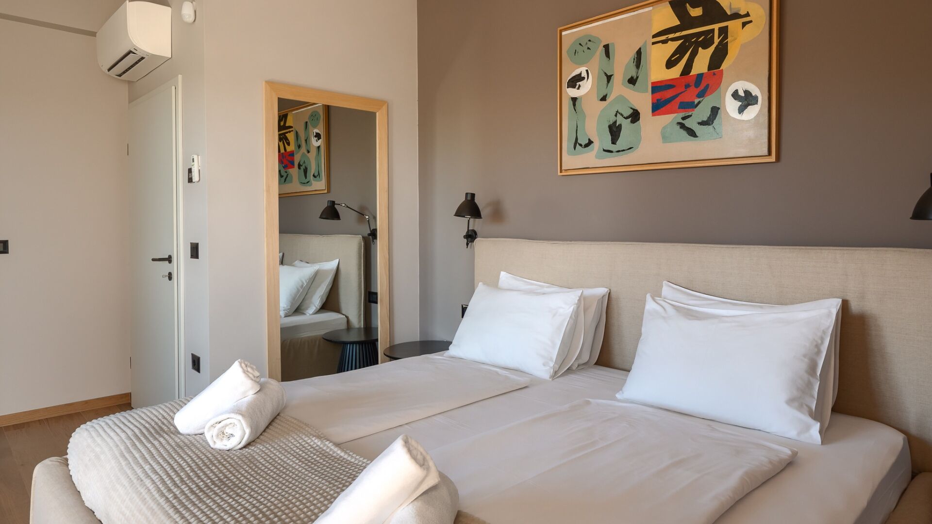 Een hotelkamer met een bed, nachtkastje, lamp en een muur met abstracte kunst.