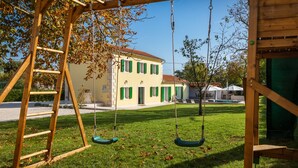 A wooden swing set with a ladder, a grassy yard, and a yellow building with green shutters. - Villa Corticum Otium by Villas Guide (Kringa)