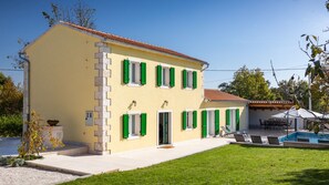 A two-story building with a yellow facade, green shutters, and a swimming pool in the background. - Villa Corticum Otium by Villas Guide (Kringa)