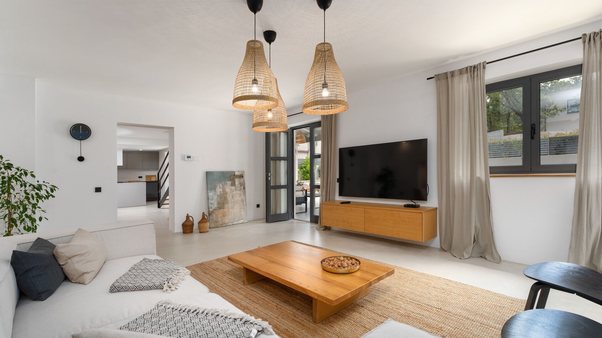 En moderne stue med sofa, sofabord og tv. Et spiseområde med bord og stole er synligt gennem en åben dør.