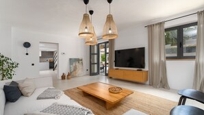 A modern living room with a sofa, coffee table, and TV. There is a dining area with a table and chairs visible through an open door. - Villa Molindrio by Villas Guide (Porec)